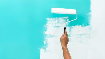 Woman's hand painting over blue wall with white paint
