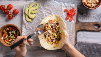 person's hands filling a tortilla to make a burrito at home