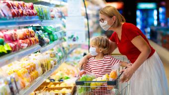 mother and child grocery shopping while wearing masks