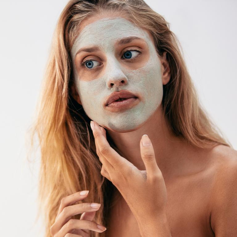woman looking in mirror with clay face mask on